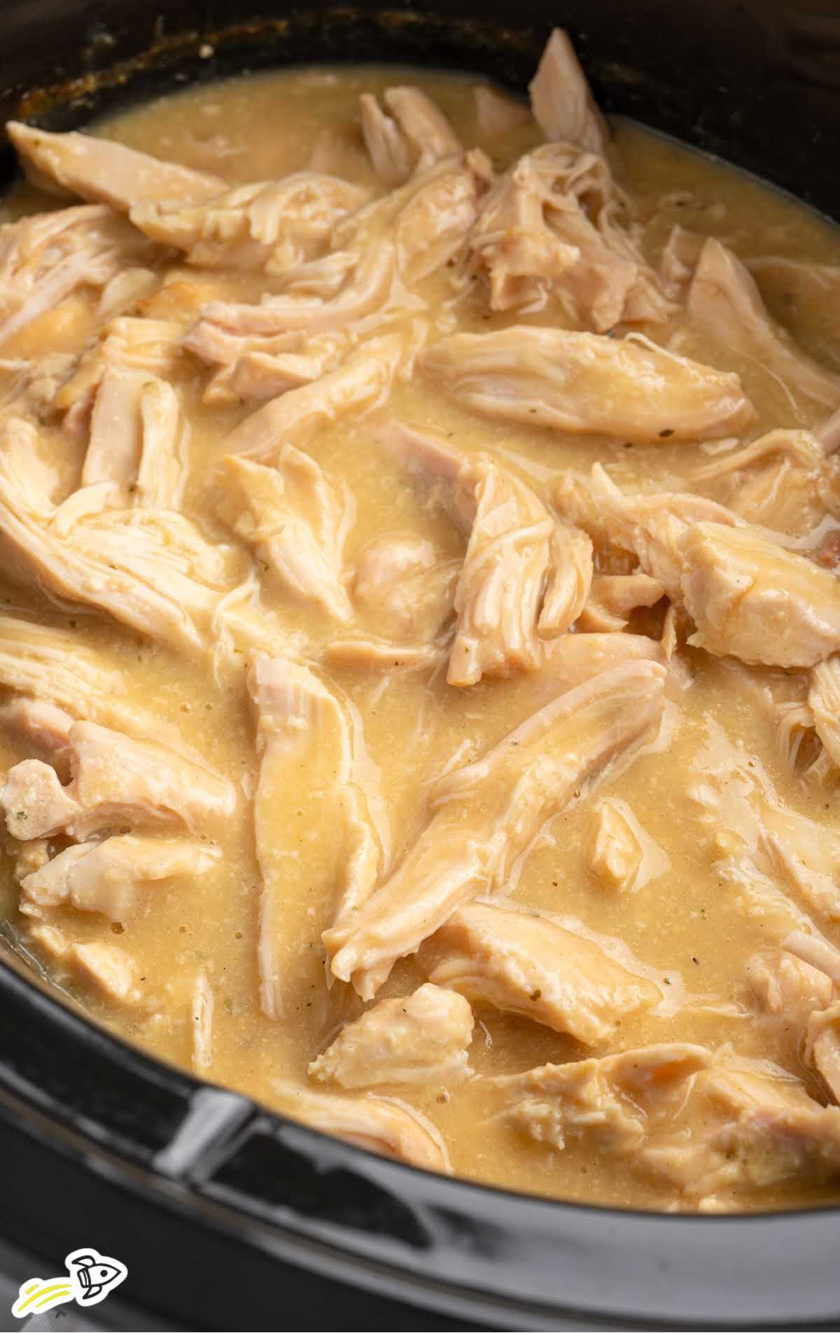Crockpot full of shredded chicken in thick golden gravy.