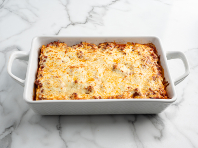 A rectangular white baking dish filled with delicious Lasagna Roll Ups, topped with melted golden-brown cheese, sits on a white marble surface.