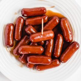 crockpot cocktail links coated in a bbq sauce and grape jelly mix served on a white plate with a toothpick
