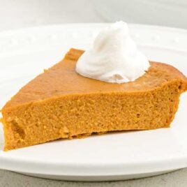 close up shot of a slice of crustless pumpkin with a dollop of cream on a white plate with a fork
