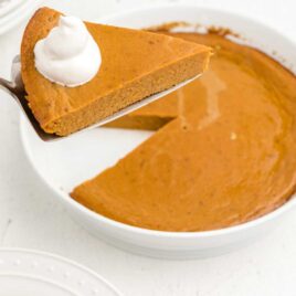 close up shot of a slice of crustless pumpkin with a dollop of cream on top being removed from the pie
