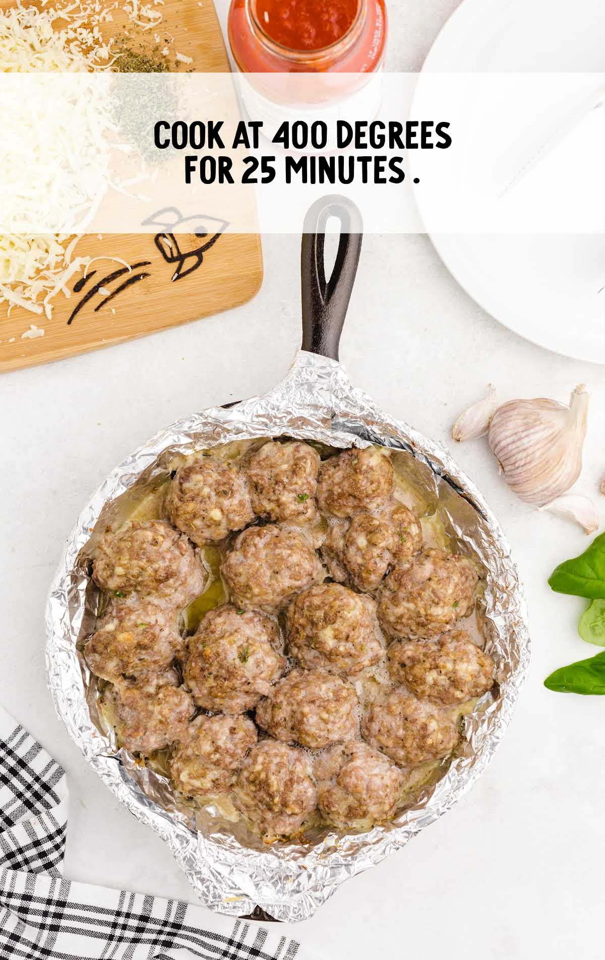 Baked meatballs in foil-lined skillet after 25 minutes of cooking, with overlay text: 'Cook at 400 degrees for 25 minutes.'
