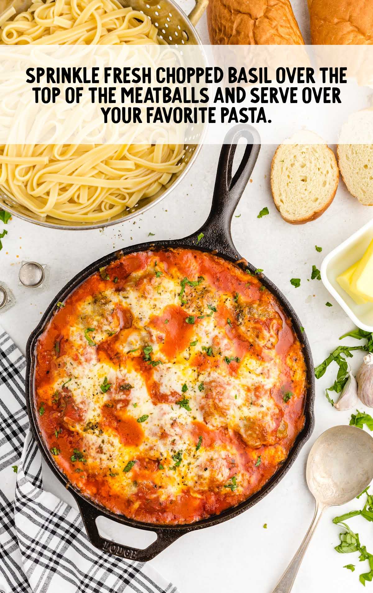 Fully baked meatball parmesan in a skillet garnished with fresh basil, pasta and bread in background, with overlay text: 'Sprinkle fresh chopped basil over the top of the meatballs and serve over your favorite pasta.'