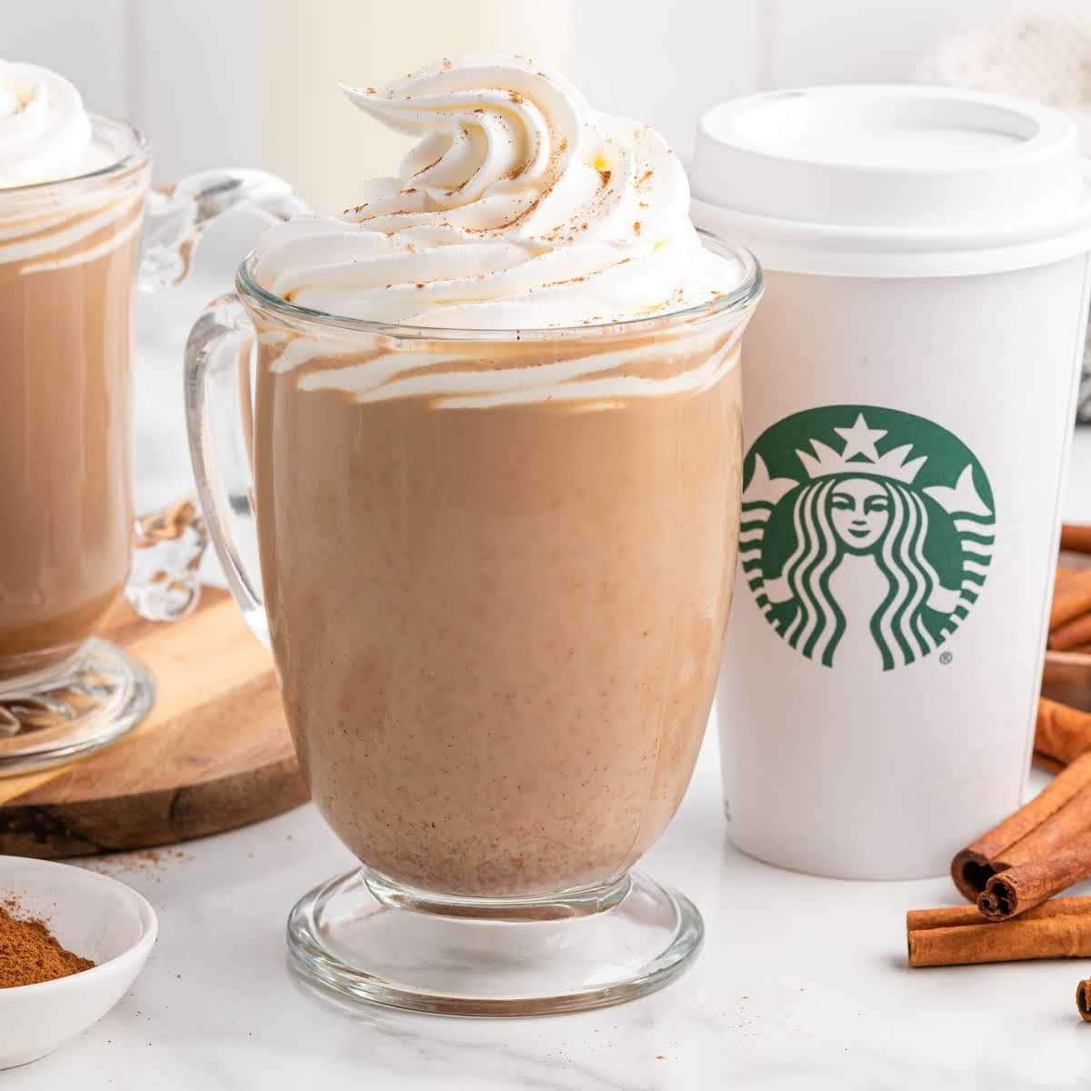 Close-up of a glass mug filled with pumpkin spice latte and topped with whipped cream, next to a Starbucks to-go cup.