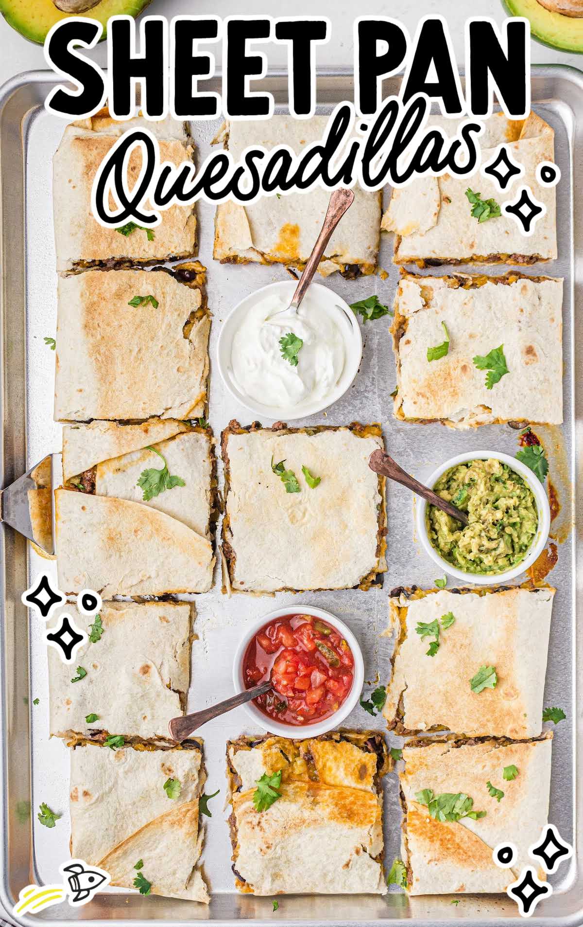 close up overhead shot of quesadillas with cups of salsa, sour cream, and guacamole on a sheet pan