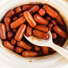 close up shot of crockpot cocktail links coated in a bbq sauce and grape jelly mix on a white spoon