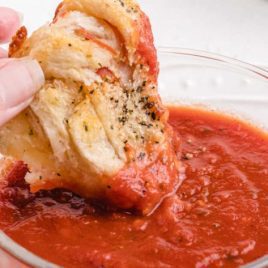 close up shot of easy pepperoni rolls being dipped into a small bowl of tomato sauce