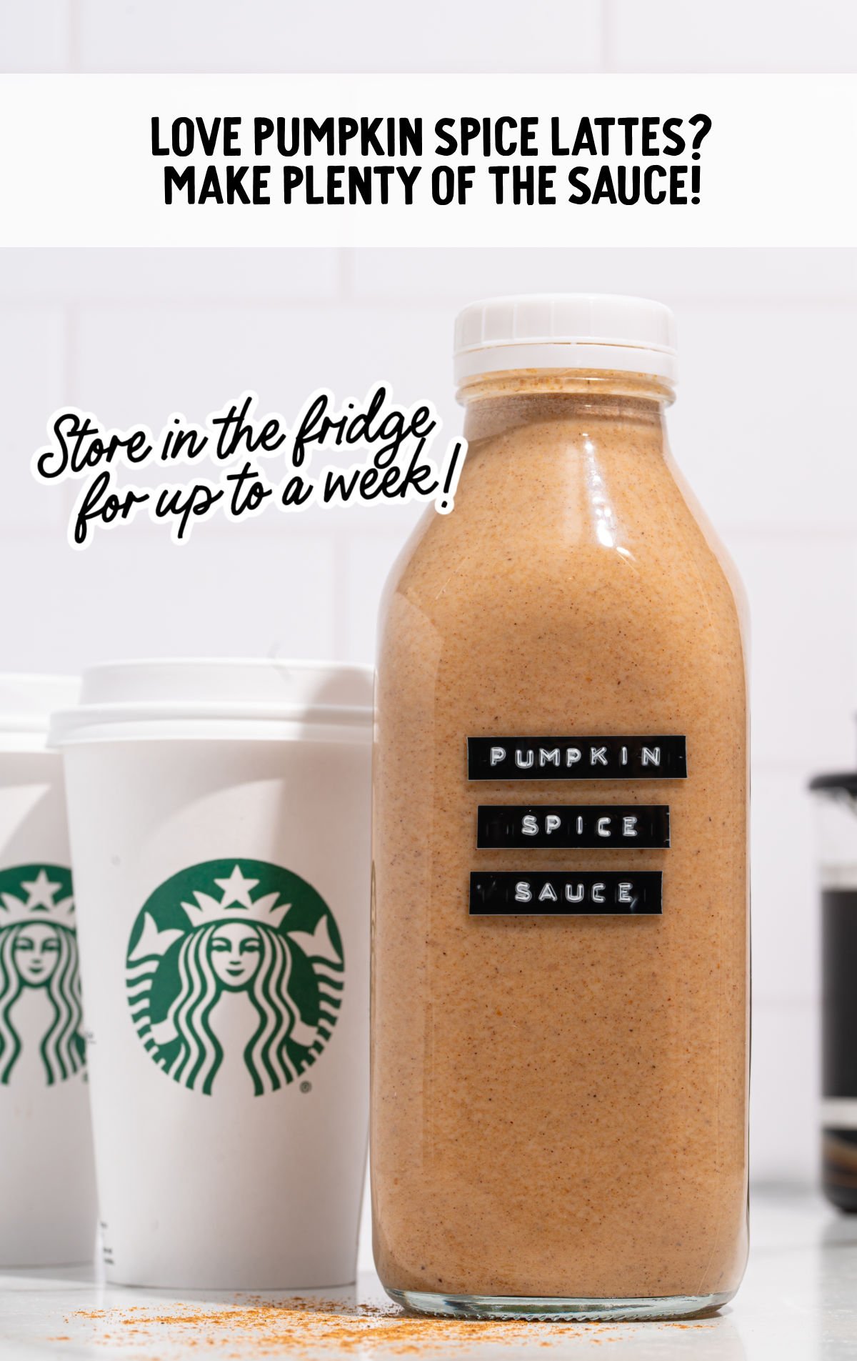 Glass bottle filled with homemade pumpkin spice sauce, labeled “Pumpkin Spice Sauce,” with Starbucks cups in the background. Text overlay reads “Love pumpkin spice lattes? Make plenty of the sauce! Store in the fridge for up to a week!”