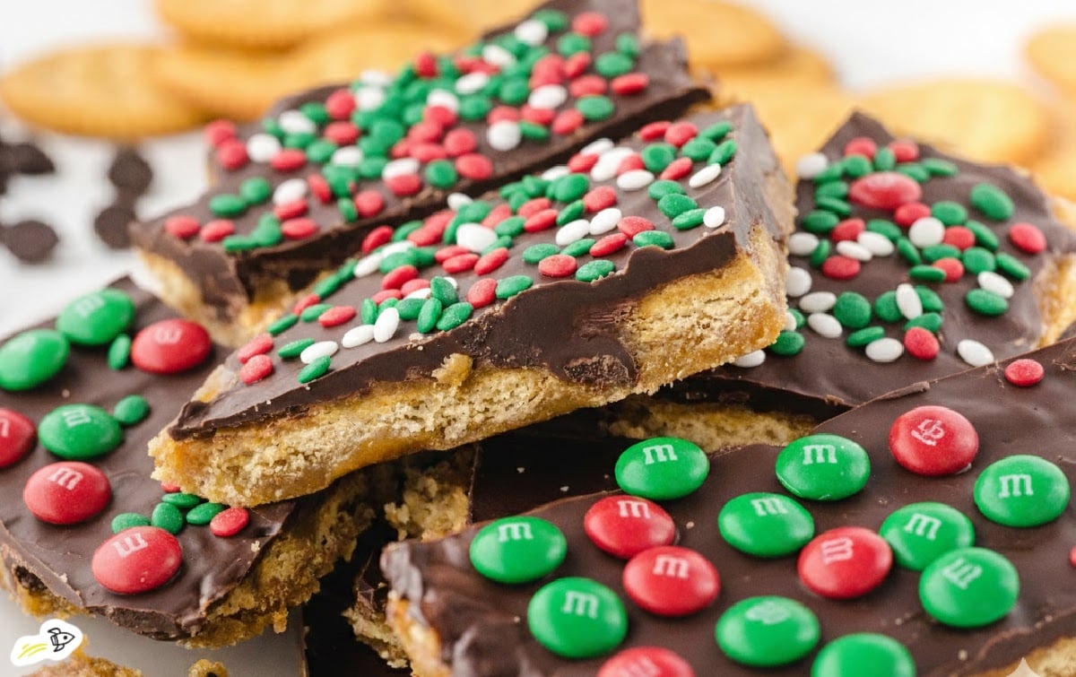Stacked pieces of Christmas Ritz cracker toffee topped with melted chocolate, red and green M&M’s, and holiday sprinkles, showing the golden buttery cracker toffee layers.