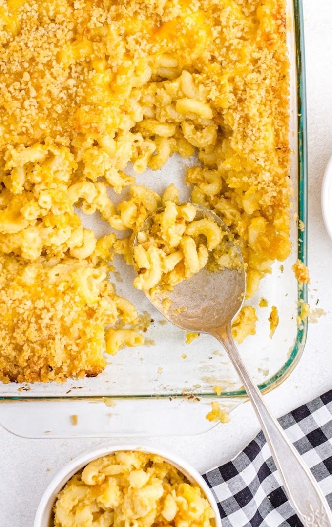 overhead shot of baked mac and cheese in a clear pan with a serving placed in a white bowl by a large spoon