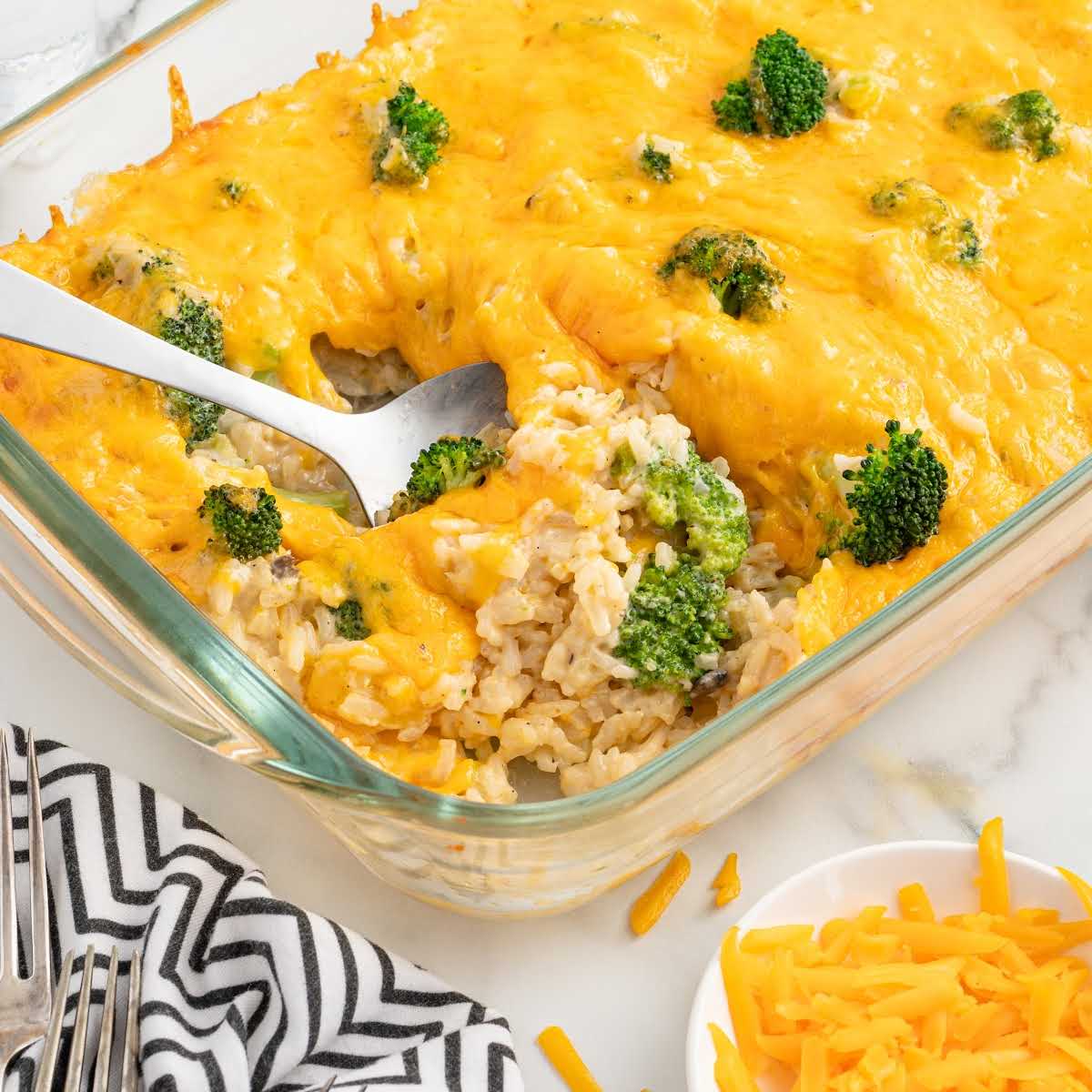 Spoonful of broccoli rice casserole with gooey melted cheddar in a glass casserole dish.