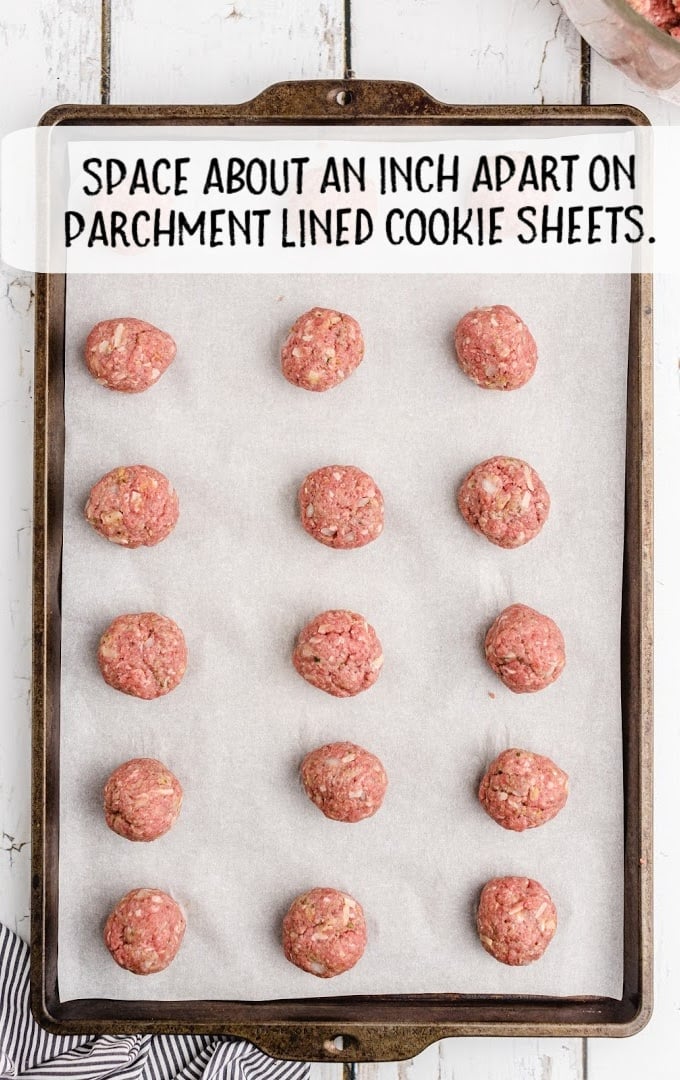 meatball mixture spread apart on a parchment lined cookie sheet