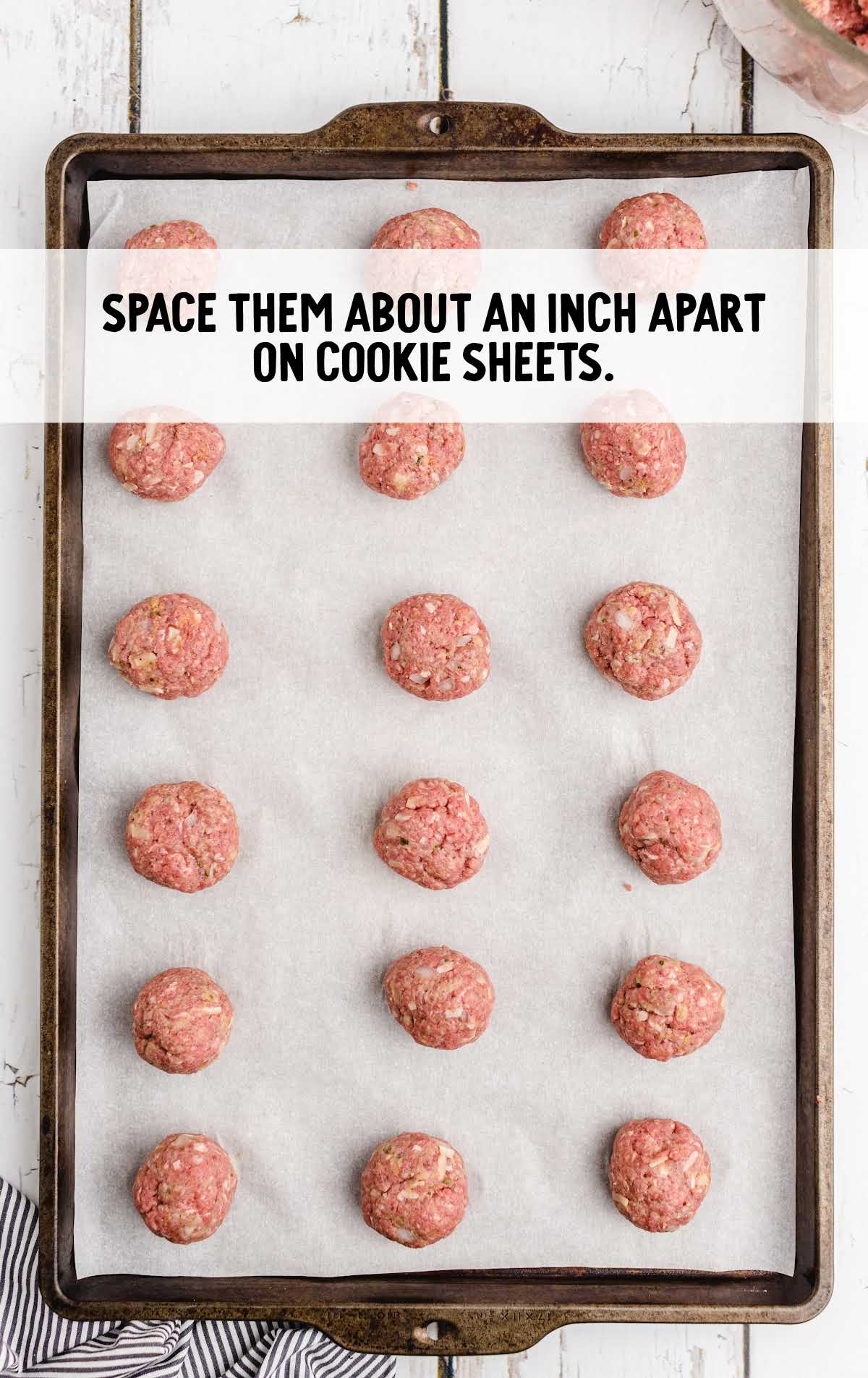 Raw meatballs spaced evenly on a baking sheet, ready for the oven.