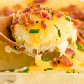 close up shot of mashed potato casserole in a clear pan being picked up with a wooden spoon