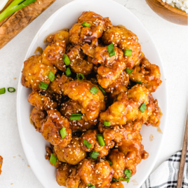 sticky sesame cauliflower garnished with green onions and toasted sesame seeds served on a white plate