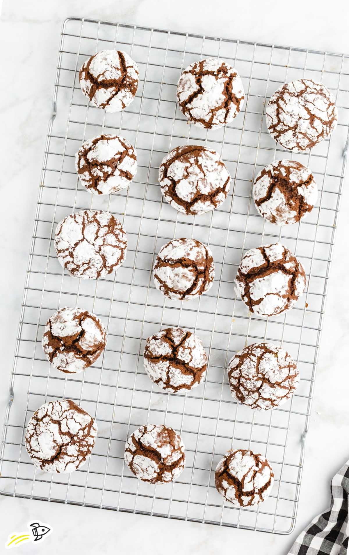 Overhead view of multiple chocolate crinkle cookies arranged on a cooling rack over a marble surface.