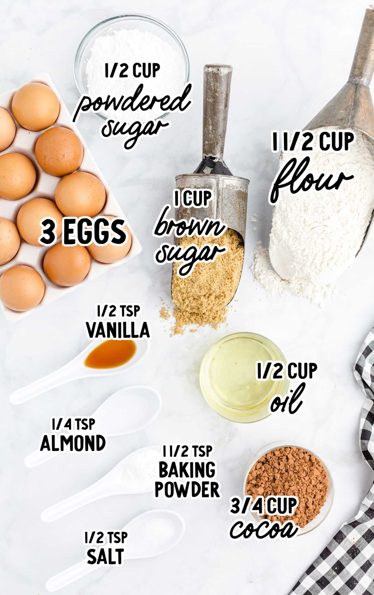 Flat lay of labeled ingredients for chocolate crinkle cookies, including cocoa powder, flour, eggs, powdered sugar, brown sugar, and vanilla.
