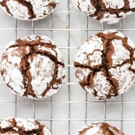 Overhead close-up of chocolate crinkle cookies on a cooling rack, showing their signature cracked appearance and powdered sugar coating.