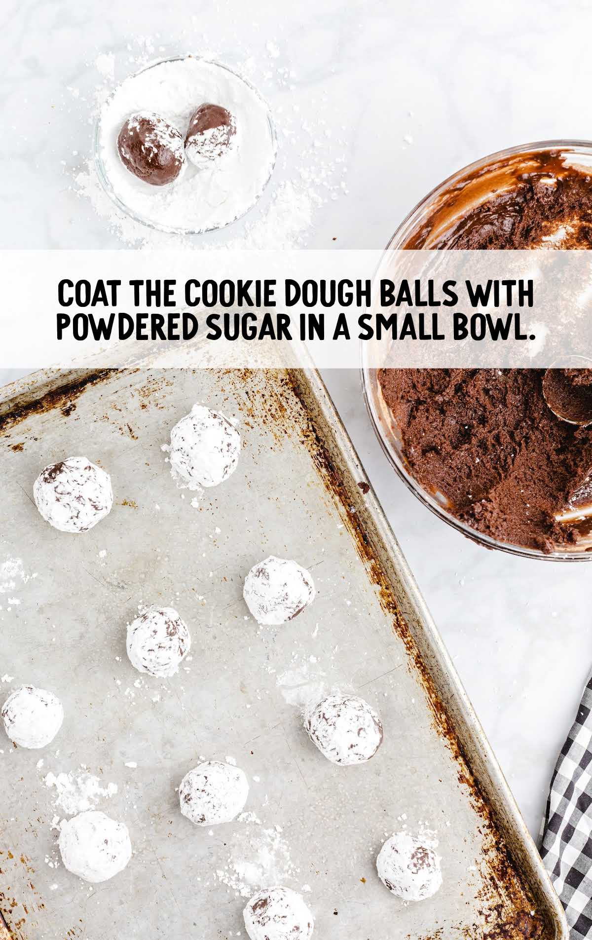 Chocolate cookie dough balls being rolled in powdered sugar in a bowl, with text overlay: “Coat the cookie dough balls with powdered sugar in a small bowl.”