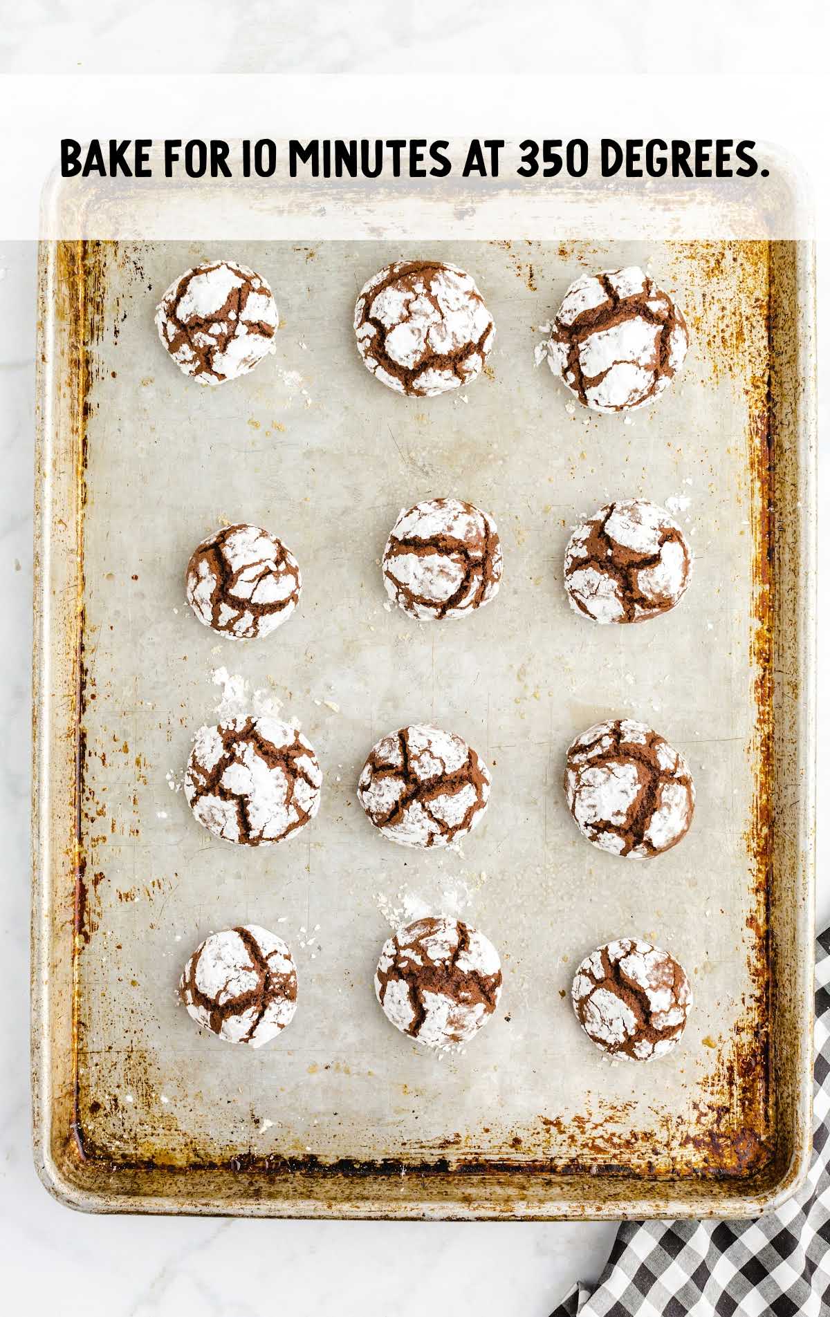 Baked chocolate crinkle cookies on a baking sheet, showing signature cracks, with text overlay: “Bake for 10 minutes at 350 degrees.”