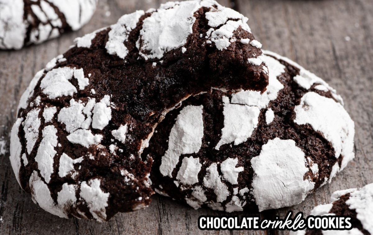 Chocolate crinkle cookies dusted with powdered sugar and cracked tops on a rustic wooden table.
