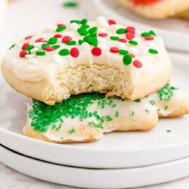 close up shot of Christmas Sugar Cookies on top of each other on a plate with one having a bite taken out of it