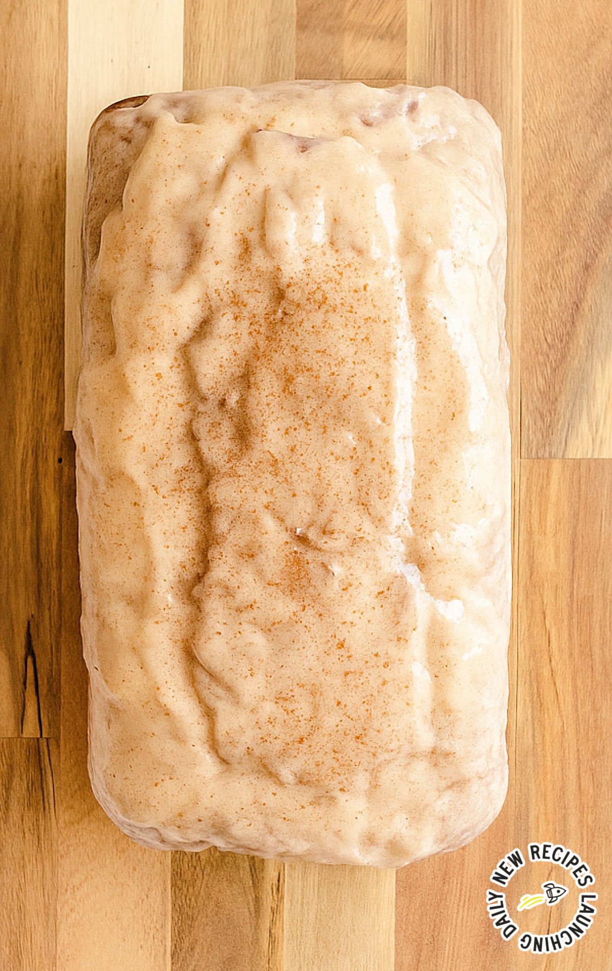 Overhead view of a whole eggnog bread loaf covered in creamy nutmeg glaze on a wooden board.