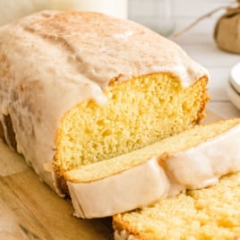 Close-up of sliced eggnog bread with thick cinnamon-nutmeg glaze on a cutting board.
