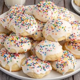Large plate of Italian cookies covered in white icing and rainbow sprinkles