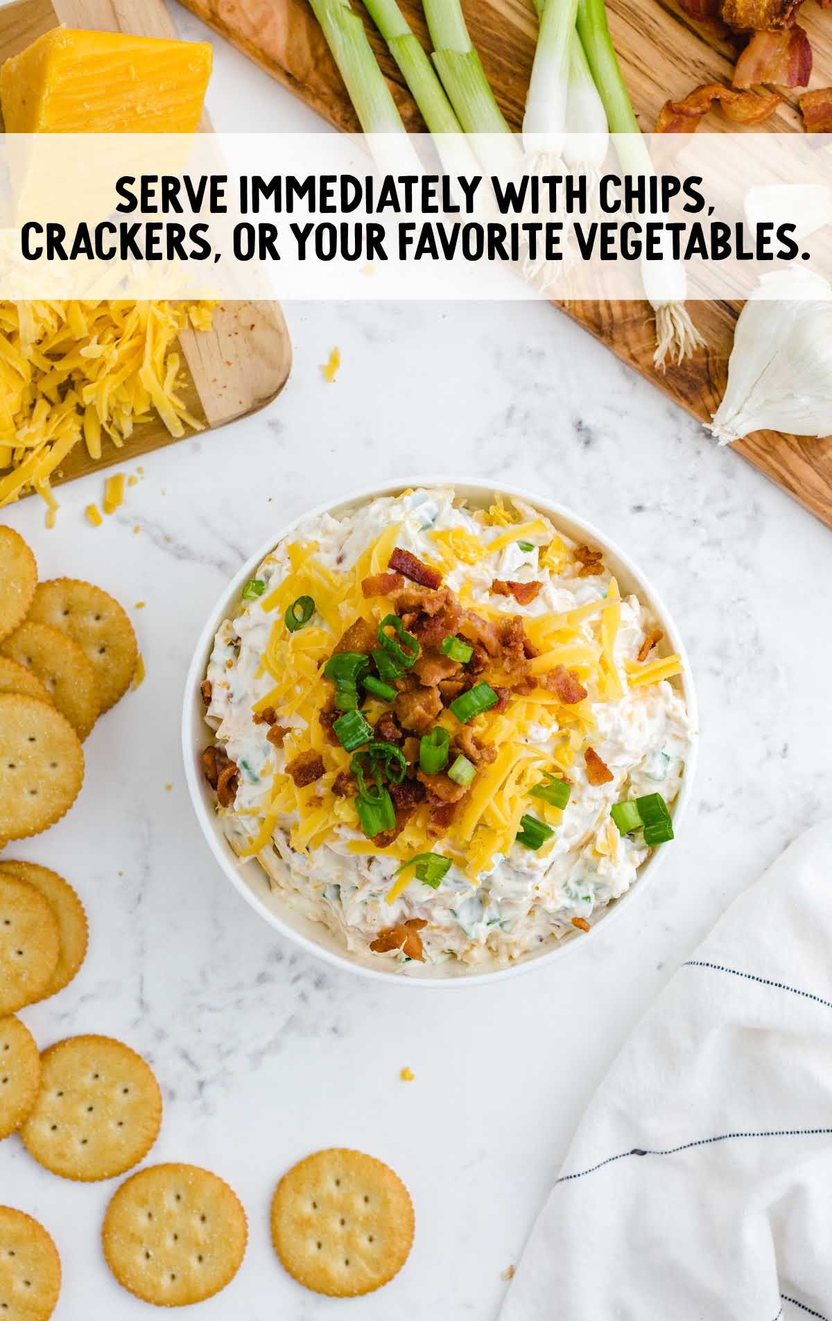 dip topped with shredded cheddar cheese, cooked bacon bits, and chopped green onions
