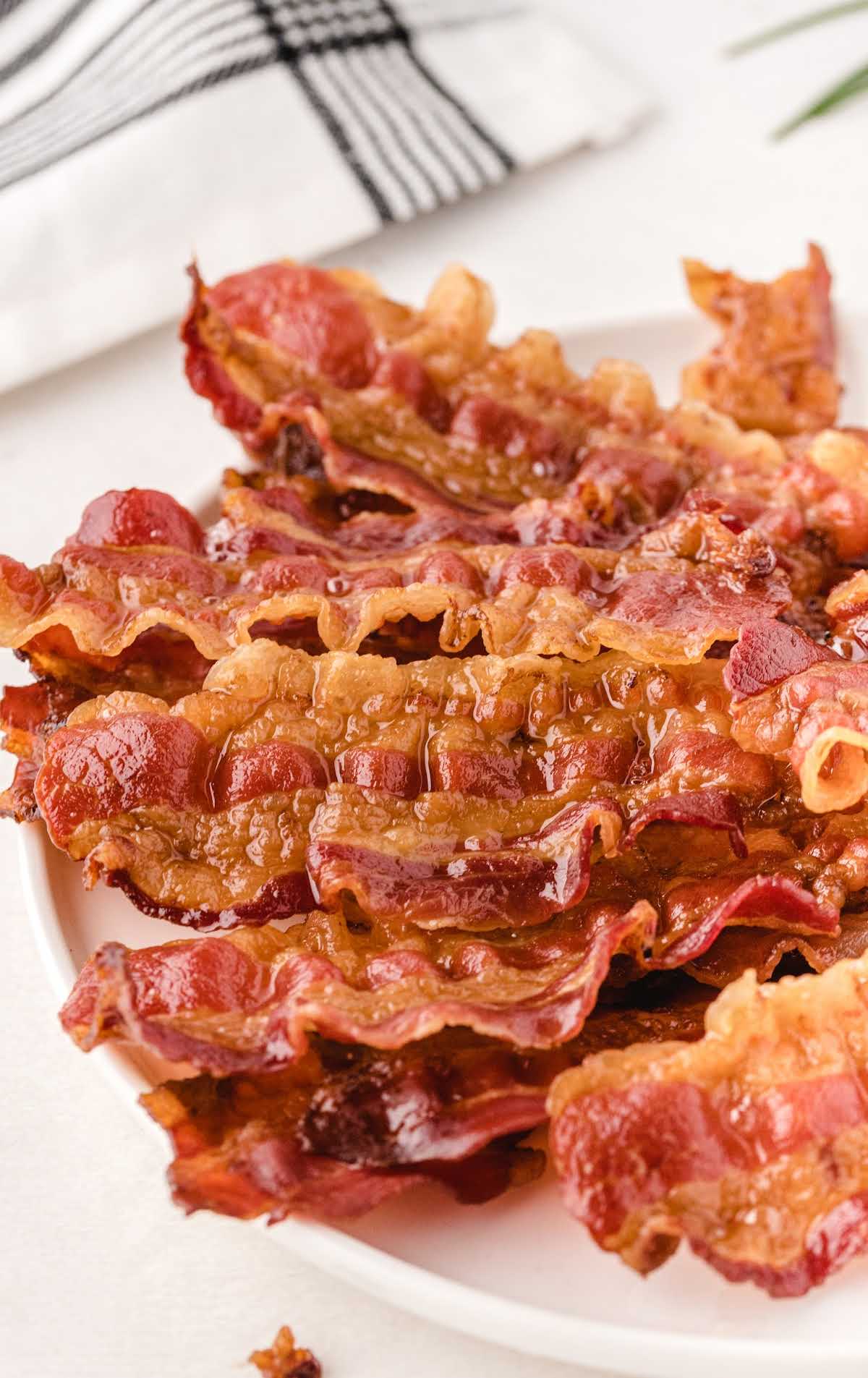 Close-up of glistening, crispy bacon pieces piled on a white plate.