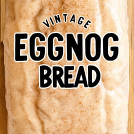 Whole eggnog bread loaf with cinnamon-spiced glaze on a wooden surface.