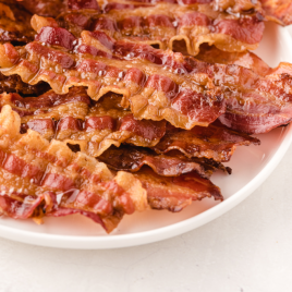 close up shot of oven baked bacon piled on top of each other on a white plate