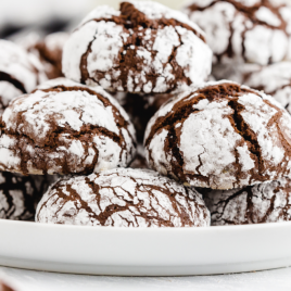 close up shot of chocolate crinkle cookies stacked on top of each other on a white tray