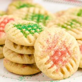 close up shot of grandma's christmas sugar cookies piled on top of each other on a white plate