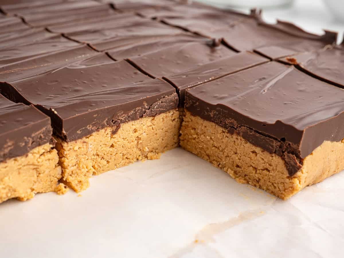 Chocolate peanut butter bars cut into squares, featuring a thick peanut butter layer on the bottom and a smooth chocolate layer on top, sitting on parchment paper—this no bake peanut butter bars recipe makes for an irresistibly easy treat.