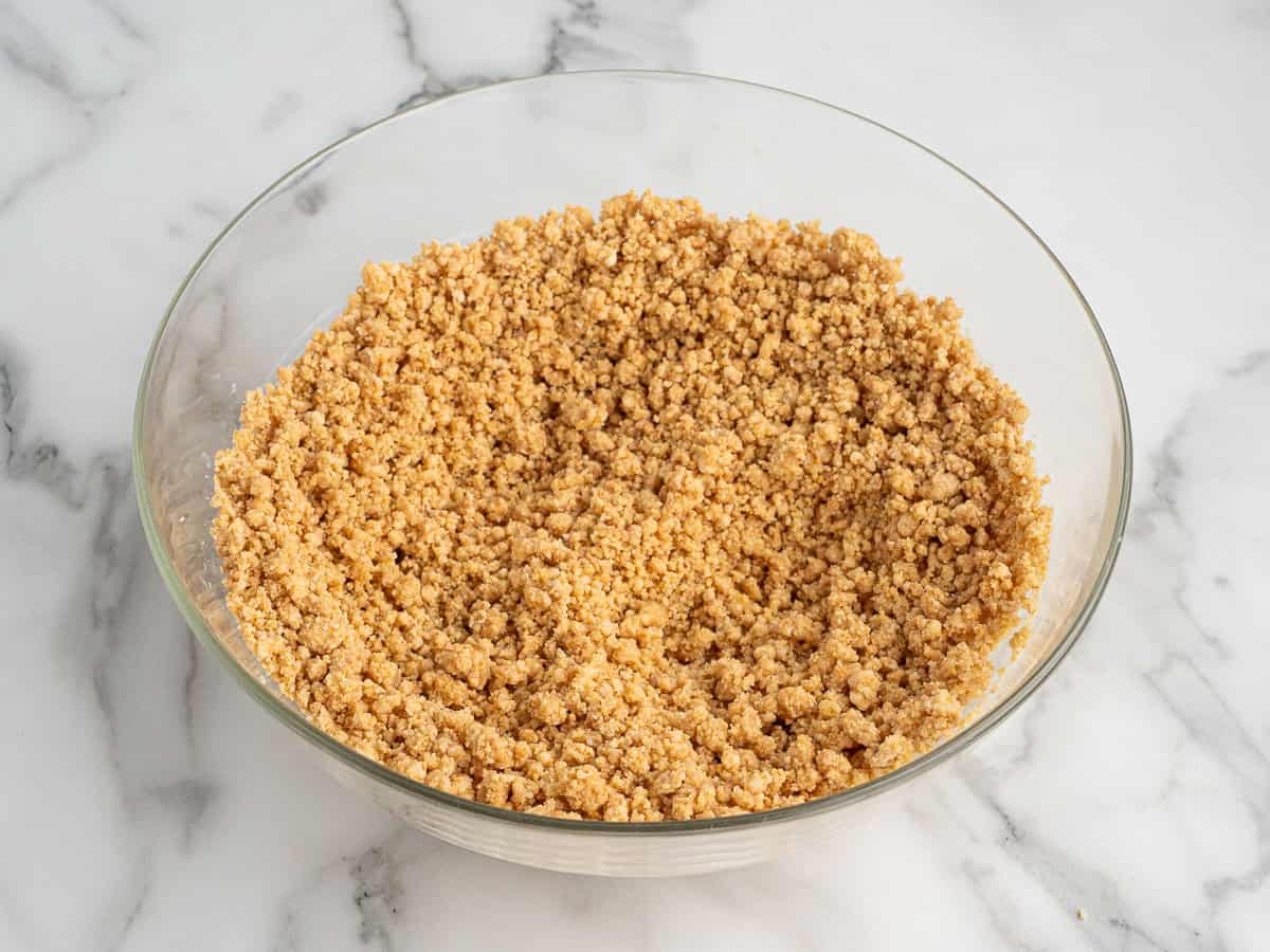 A glass bowl filled with a crumbly mixture, likely graham cracker crumbs for making delicious peanut butter bars, sits on a white marble surface.