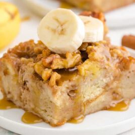 close up shot of a slice of banana bread pudding topped with banana slices on a plate