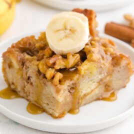 close up shot of a slice of banana bread pudding topped with banana slices on a plate