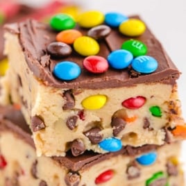 Close-up of a stacked no-bake cookie dough bar with chocolate chips, M&M's, and chocolate topping.