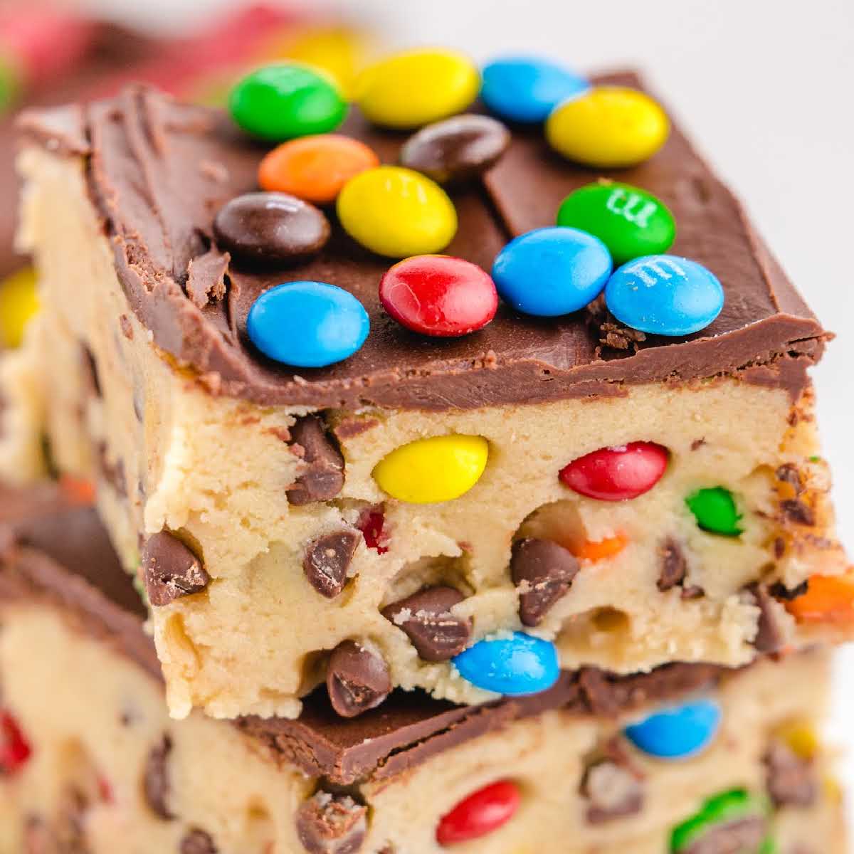 Close-up of a stacked no-bake cookie dough bar with chocolate chips, M&M's, and chocolate topping.
