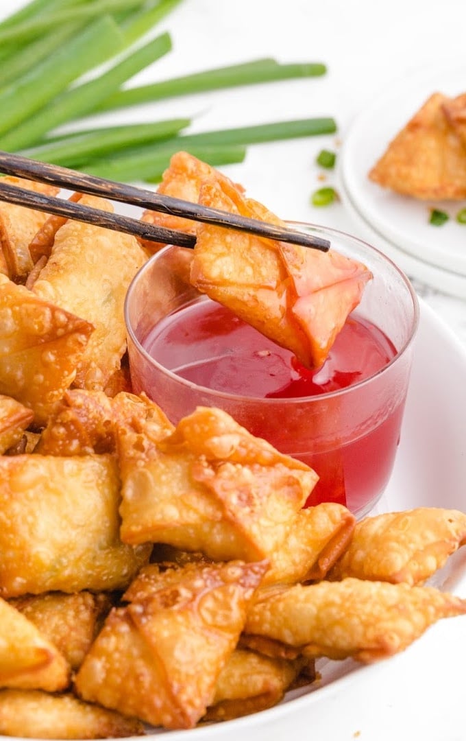 close up shot of crab rangoon being dipped in sauce with chop sticks on a white plate