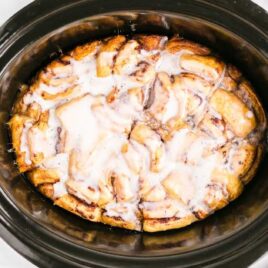 close up overhead shot of Crockpot Cinnamon Roll Casserole in a crockpot topped with icing