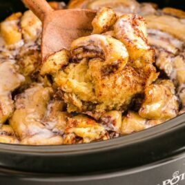 close up shot of Crockpot Cinnamon Roll Casserole in a crockpot with a large wooden spoon