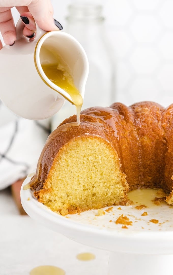 close up shot of kentucky butter cake with glaze being poured on top of it on a white stand