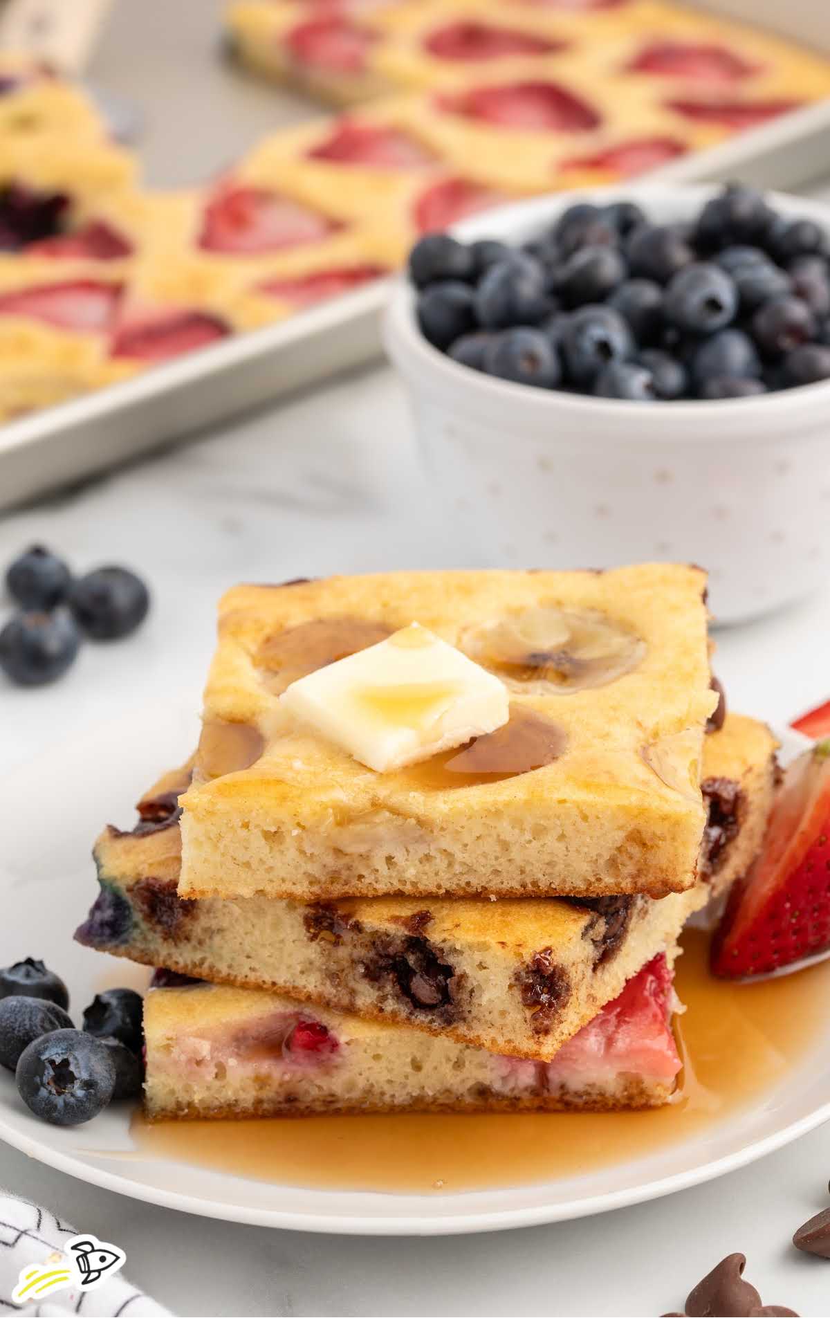 a plate of pancakes topped with a slice of butter and served with fruit