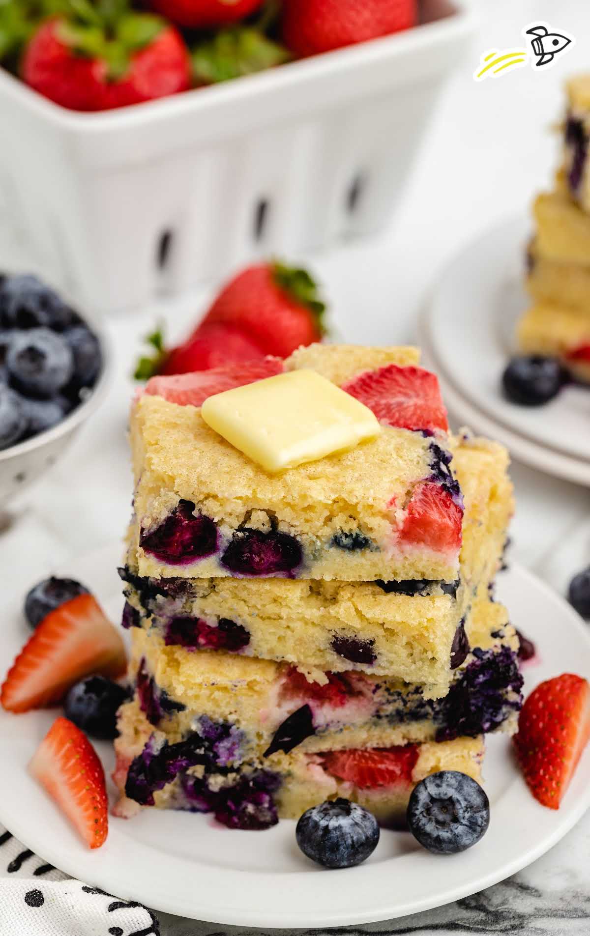 sheet pan pancakes stacked on top of each other on a white plate with fruits