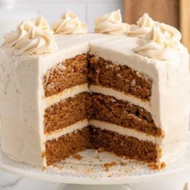 Slice of gingerbread layer cake with rich frosting served on a white plate.