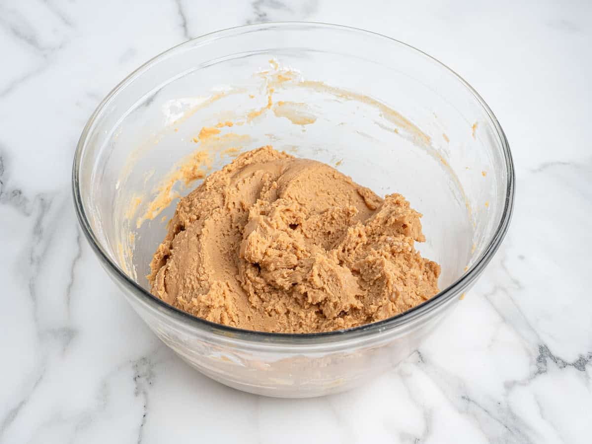 A glass bowl filled with peanut butter cookie dough sits on a white marble surface, perfect for whipping up a quick Peanut Butter Fudge (Microwave) treat.