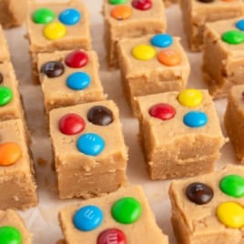 Squares of Peanut Butter Fudge (Microwave) topped with colorful candy-coated chocolates, arranged in neat rows on a sheet of parchment paper.